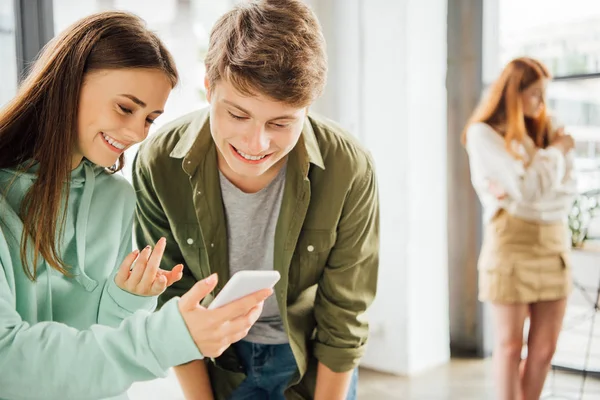 Deux amis heureux souriant tout en utilisant un smartphone à l'école — Photo de stock