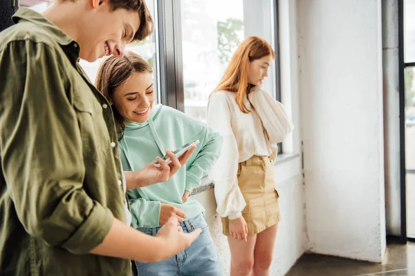 Dos amigos sonriendo mientras usan el teléfono inteligente en la escuela - foto de stock