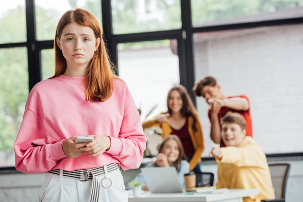 Group of schoolchildren bullying sad girl with smartphone — Stock Photo