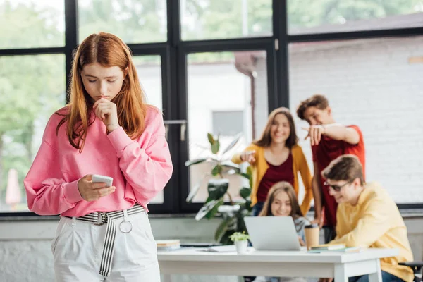 Group of schoolchildren bullying sad girl with smartphone — Stock Photo