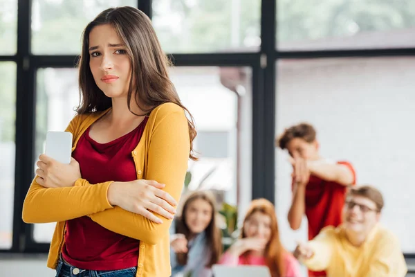 Group of schoolchildren bullying sad girl with smartphone — Stock Photo