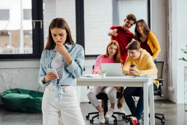 Group of schoolchildren laughing at sad girl with smartphone — Stock Photo