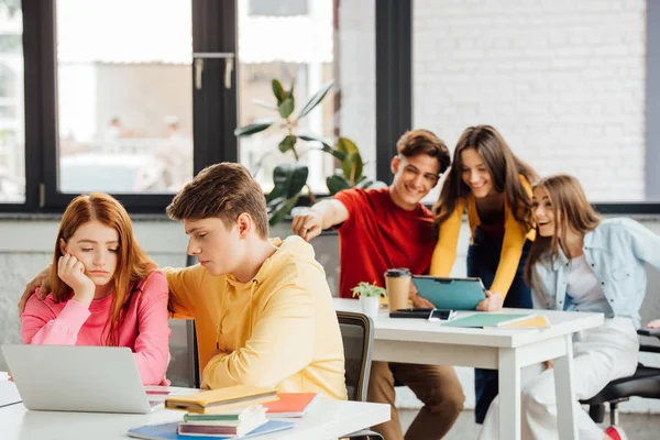 Écoliers avec tablette numérique pointant du doigt et riant de camarades de classe — Photo de stock