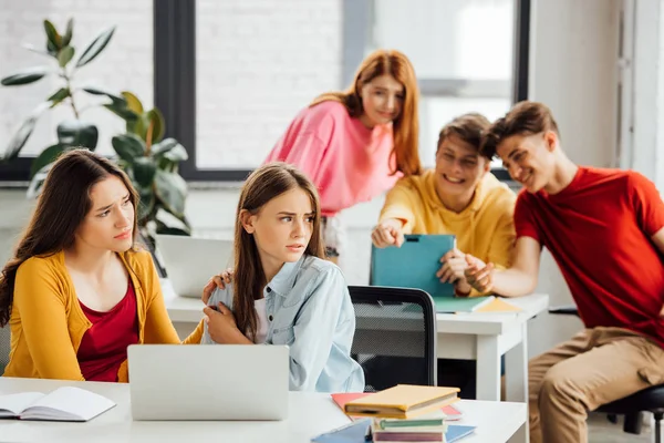 Escolares con tableta digital señalando con el dedo y riendo de sus compañeros de clase - foto de stock