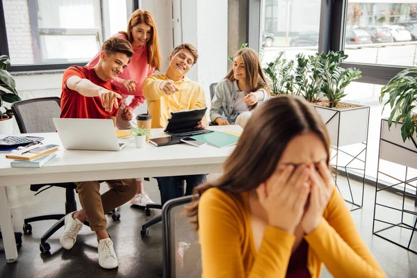 Schoolchildren laughing while bullying sad girl on foreground — Stock Photo