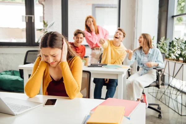 Sad girl covering ears with hands while classmates bullying her — Stock Photo
