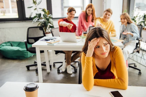 Schoolchildren laughing while bullying sad girl on foreground — Stock Photo