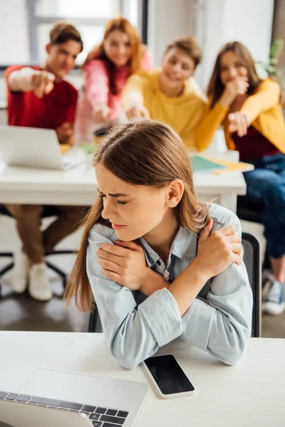 Schoolchildren laughing while bullying sad girl on foreground — Stock Photo