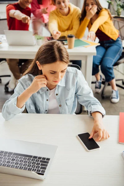 Schoolchildren laughing while bullying sad girl on foreground — Stock Photo