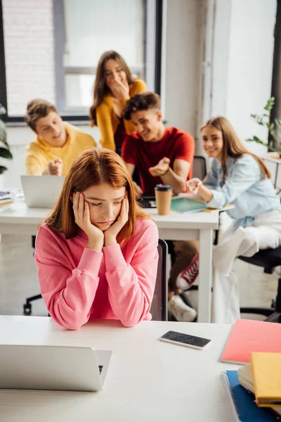 Schoolchildren laughing while bullying sad girl on foreground — Stock Photo