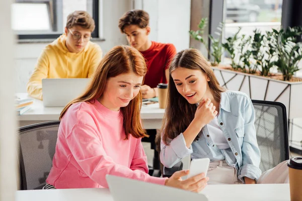 Smiling schoolchildren using laptops and smartphone in school — Stock Photo