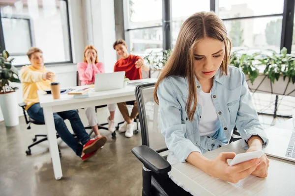 Laughing schoolchildren bullying sad girl with smartphone in school — Stock Photo