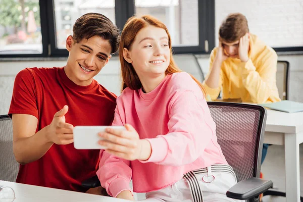 Два друга улыбаются во время использования смартфона в школе — стоковое фото
