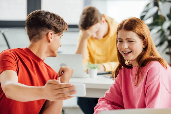 Dos amigos sonriendo mientras usan el teléfono inteligente en la escuela - foto de stock