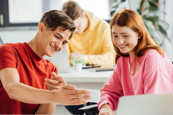 Due amici sorridenti durante l'utilizzo dello smartphone a scuola — Foto stock
