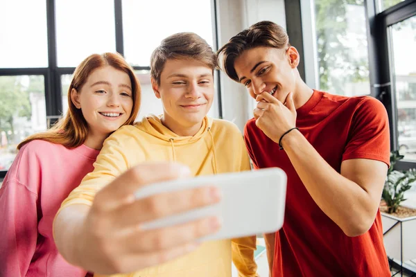 Tres amigos tomando selfie y sonriendo en la escuela - foto de stock