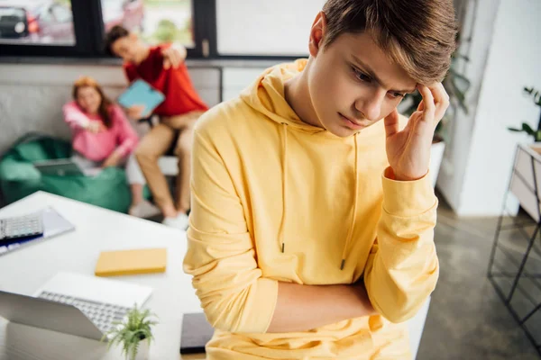 Пенсійний хлопчик в жовтому светрі і сміється однокласники знущаються над ним — стокове фото