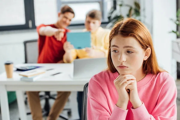 Sad pensive girl and classmates laughing at her in school — Stock Photo