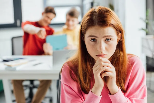 Triste menina pensativa e colegas de classe rindo dela na escola — Fotografia de Stock