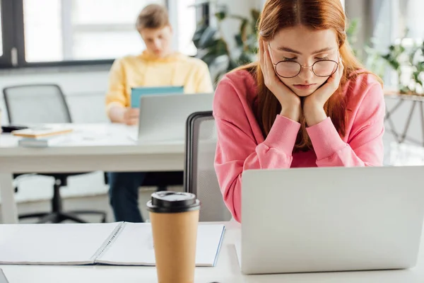 Escolares pensativos sentados em mesas e usando laptops — Fotografia de Stock