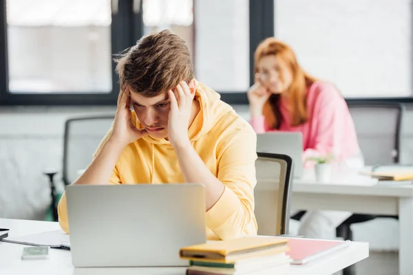 Escolares pensativos sentados en escritorios con computadoras portátiles en la escuela - foto de stock