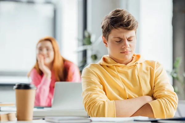 Dissatisfied boy in yellow hoodie sitting at desk in school — Stock Photo