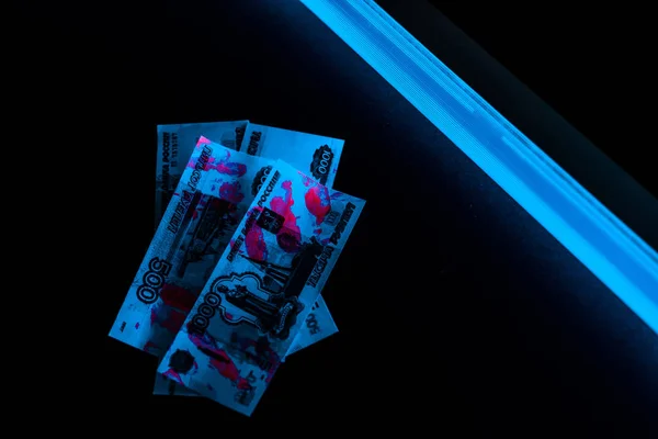 Top view of blue ultraviolet lightning on russian money on black — Stock Photo