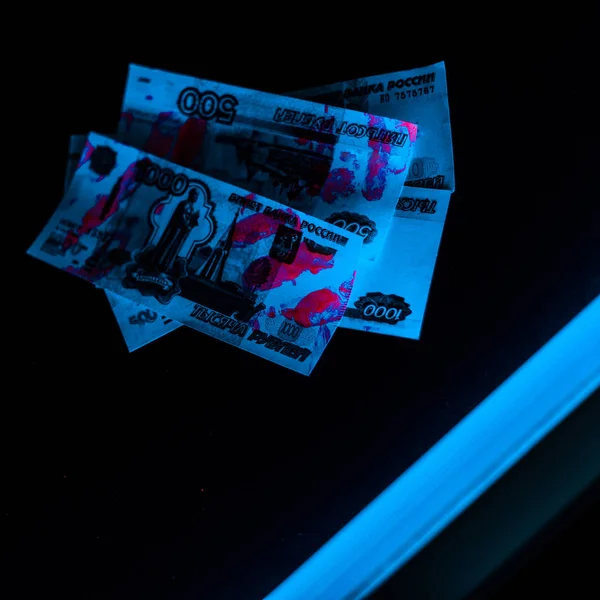 Selective focus of blue ultraviolet lightning on russian money on black — Stock Photo