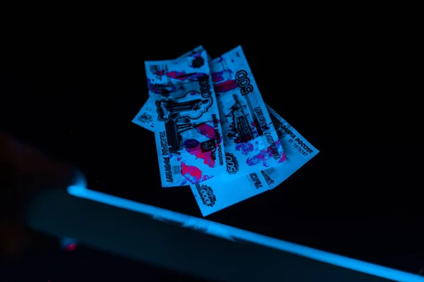 Selective focus of man holding uv lamp near russian money on black — Stock Photo