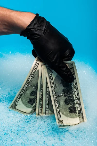 Cropped view of man in black rubber glove holding dollar banknotes — Stock Photo