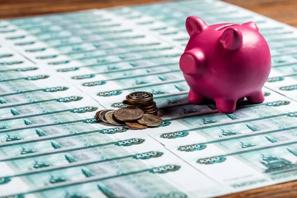 Selective focus of pink piggy bank near metallic coins on russian money — Stock Photo