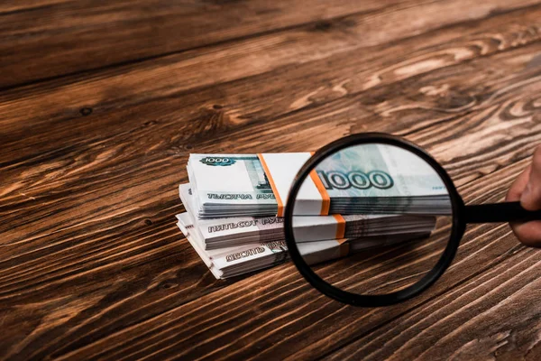 Vista cortada do homem segurando lupa perto do dinheiro russo na mesa — Fotografia de Stock