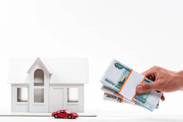 Cropped view of man holding russian money near toy car and carton house on white — Stock Photo