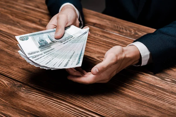 Cropped view of man holding russian banknotes near wooden table — стокове фото