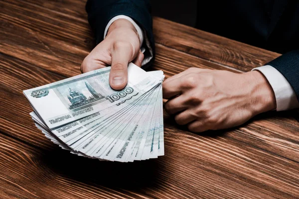 Cropped view of man holding russian money near wooden table — Stock Photo