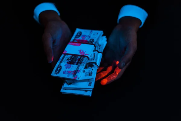 Обрізаний вид людини, що тримає хабар під ультрафіолетовим освітленням ізольовано на чорному — стокове фото