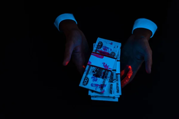 Vista cortada do homem segurando suborno sob iluminação uv azul isolado em preto — Fotografia de Stock