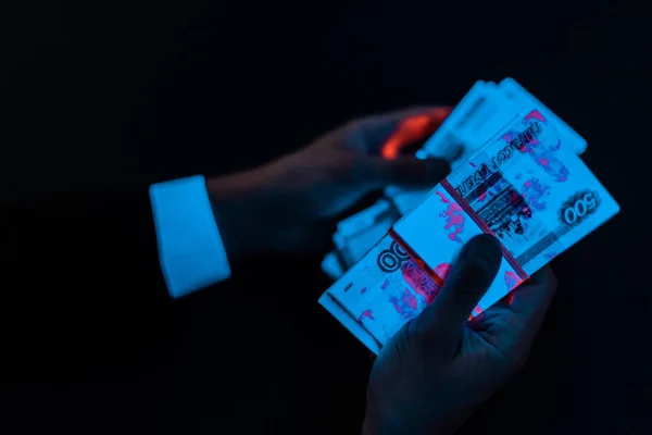 Cropped view of man holding russian money under blue uv lighting isolated on black — Stock Photo