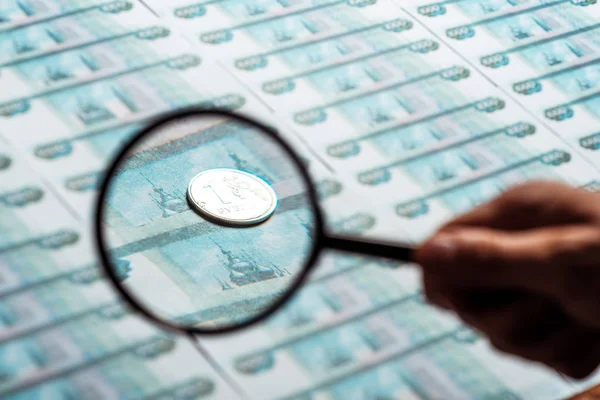 Selective focus of man holding magnifying glass near silver coin on russian money — Stock Photo