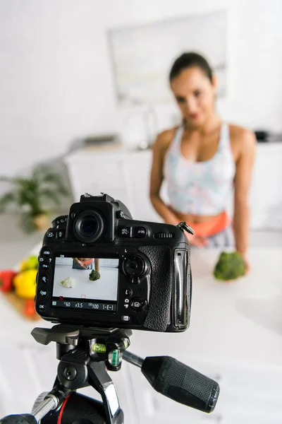 Selective focus of digital camera with sportswoman gesturing near vegetables — Stock Photo