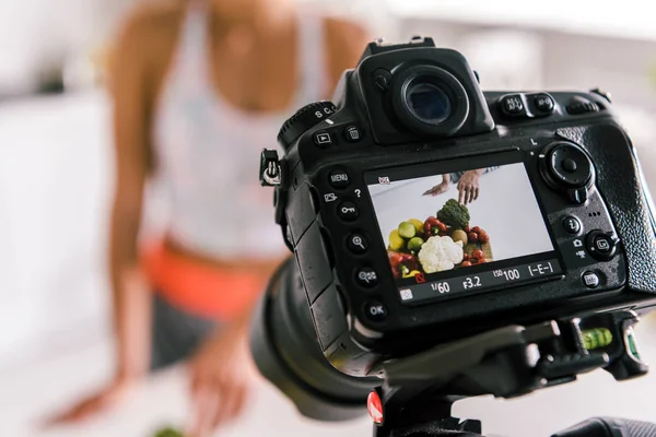 Foco seletivo da câmera digital com esportista gestos perto de vegetais na tela — Fotografia de Stock