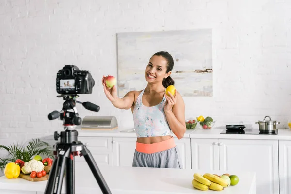 Selective focus of happy woman holding fruits near digital camera — Stock Photo