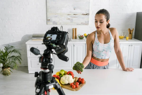 Selective focus of sportswoman holding broccoli near digital camera — Stock Photo
