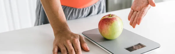 Panoramic shot of woman gesturing near food scales and apple — Stock Photo
