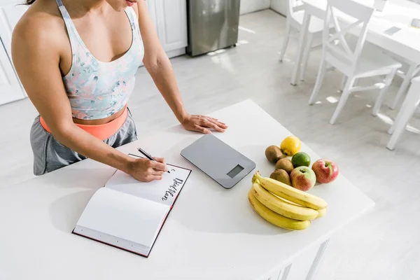 Cropped view of woman holding pen near notebook with lettering and fruits — Stock Photo