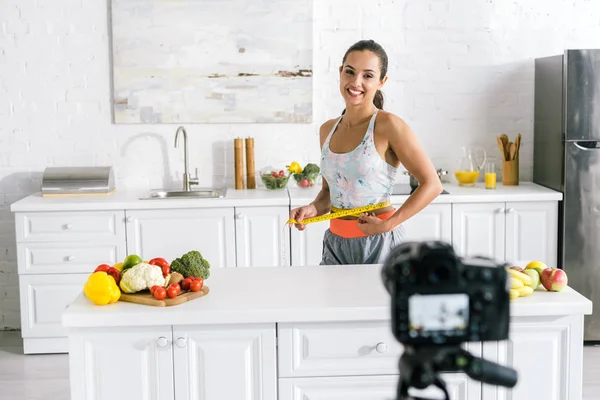 Selektiver Fokus der glücklichen Frau, die Taille misst und auf die Digitalkamera blickt — Stockfoto