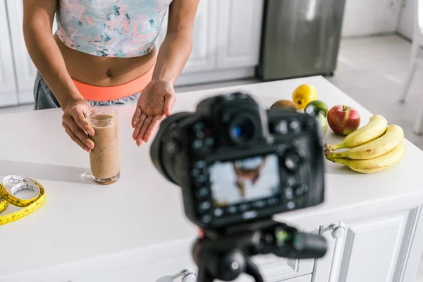 Selective focus of girl gesturing near glass with smoothie and digital camera — Stock Photo