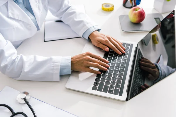 Vista recortada del médico escribiendo en el ordenador portátil con pantalla en blanco - foto de stock