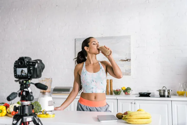 Foco seletivo de menina beber smoothie perto da câmera digital — Fotografia de Stock