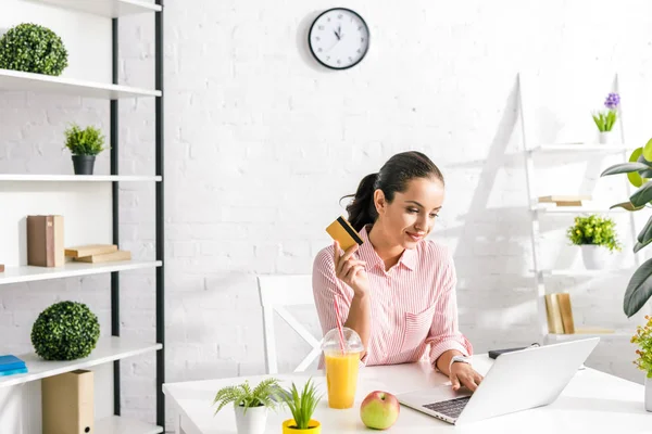 Menina atraente usando laptop e segurando cartão de crédito — Fotografia de Stock